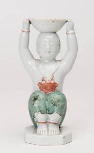 A Chinese porcelain figural candlestick, modelled as a seated boy with a bowl on his head, decorated in low-fired red & turquoise enamels 18th Century