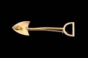 A Miner's brooch, a shovel with diamond set nugget, yellow gold, length 49mm. (Similar example lot 389, sold June 3, 2014, Mossgreen Australian & Colonial Antique & Historical)