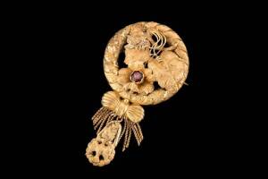 A gold wreath and foliate brooch by Lamborn and Wagner, Melbourne, set with a garnet and supporting a tassel and dove drop. Yellow gold. Marked L & W, with crown marks. Diameter 37mm, length 68mm.