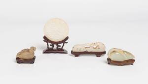 A group of four jade carvings; a white jade dragon, 20th Century; a pair of carved jade mandarin ducks, 20th Century; a celadon jade goose, 20th Century; a jade carved round pendant with flowers and fruits on a wooden stand. The pendant 6cm diameter