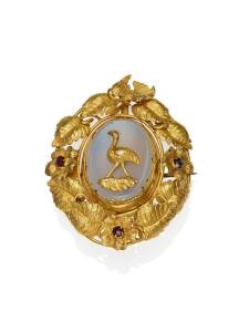 A gold and quartz brooch, possibly New Zealand, the oval brooch with revolving quartz panel, one side depicting a flightless bird, set within a leaf and tendril frame, with garnet set flowers and bird surmount. Yellow gold. Weight 23.38 grams. Length 5.3c