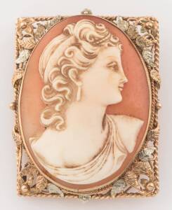 A vintage helmet shell cameo brooch, the oval cameo depicting a classical female profile, in a rectangular two tone foliate mount. 9ct yellow and white gold. Weight 15 grams. Length 4.2cm.