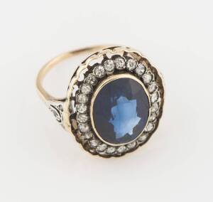 A synthetic blue sapphire and diamond ring, the oval blue stone surrounded by single and old cut diamonds in a scalloped setting. 14ct yellow gold. Weight 5.54 grams. Size O.