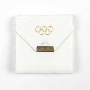 IOC OLYMPIC PARTICIPANT'S BADGE, Olympic Torch badge dated "1956", affixed to card "Games of the XVIth Olympiad, 1956, Participant, 102474", in white presentation wallet with Olympic rings on front. {We have previously sold these badges for Shirley Strick
