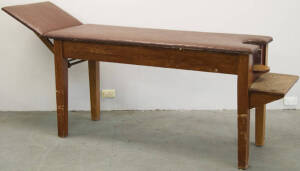 Padded wooden table with operable head support and shelving at the foot end.