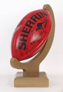 OVERSIZE "SHERRIN" FOOTBALL, from c1995 Bob Shearer Golf Classic, with 24 signatures including Ted Whitten, Bob Shearer, Garry "Buddha" Hocking, Russell Mark & Sandra Mackenzie-Wood, with wooden display stand.