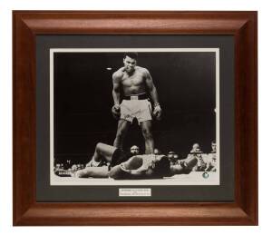 MUHAMMAD ALI, signed b/w photograph of Ali standing over Sonny Liston (signature with slight fading), window mounted, framed & glazed, overall 77x67cm. With CoA.