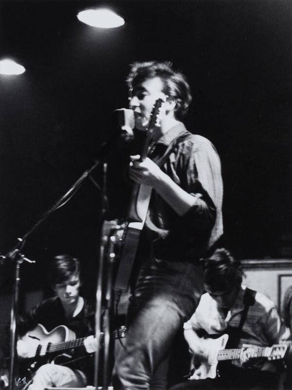 THE BEATLES: Photograph "John Lennon sings and plays guitar with Stuart Sutcliffe and George Harrison at the Top Ten club in Hamburg, 1961", by Peter Bruchmann, initialled "P.B" lower left, window mounted, framed & glazed, overall 59x69cm.