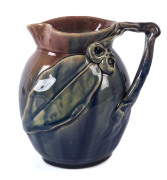 REMUED POTTERY Jug with applied gumnuts, leaf and branch handle glazed in pink, blue and mauve