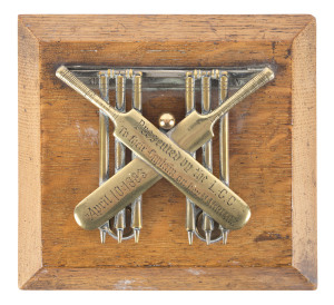 Mounted brass desk-top paper holder comprised of crossed cricket bats in front of a pair of wickets with a cricket ball at centre; the whole mounted on a wooden base; the bats engraved "Presented by the L.C.C. [Ladies Cricket Club] To their Captain on her