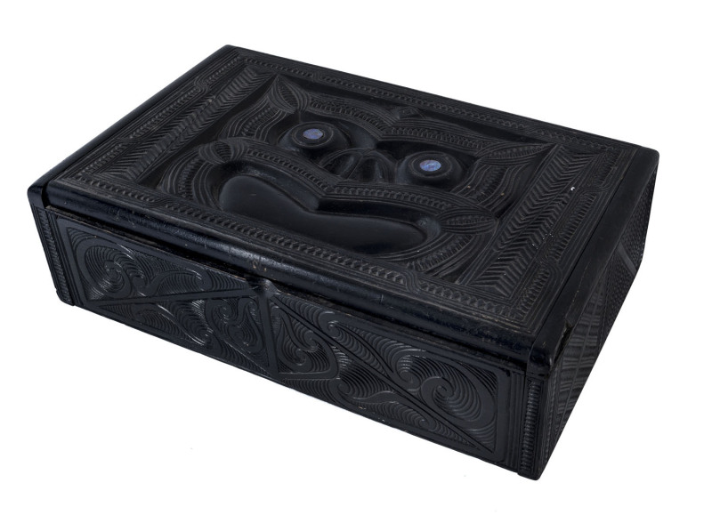 An ebonized wooden box, carved with Maori decorations and with inlaid paua shell eyes, late 19th century, 