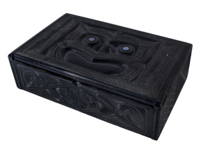 An ebonized wooden box, carved with Maori decorations and with inlaid paua shell eyes, late 19th century,