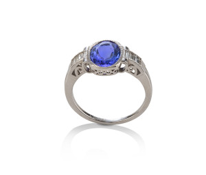 An 18ct white gold ring featuring an oval faceted purplish-blue tanzanite, millegrain rims set in a pierced oval box mount and flanked to the side by three baguette diamonds, stamped "750"