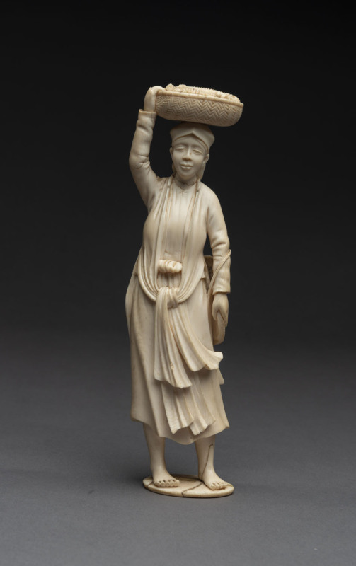 A carved ivory figure of a peasant carrying a basket of corn, 19th century, ​20cm high