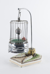 Birdcage singing bird novelty clock, nickel plated, suspended on a floral porcelain base, early 20th century, 26cm high