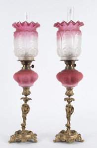 A pair of antique piano sconce kerosene oil lamps with ruby glass fonts and shades and gilt metal stands, 19th century, 55cm high