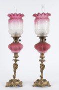 A pair of antique piano sconce kerosene oil lamps with ruby glass fonts and shades and gilt metal stands, 19th century, ​55cm high