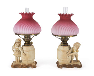 A pair of German figural bisque porcelain kerosene lamps with ruby glass shades, 19th century, 34cm high