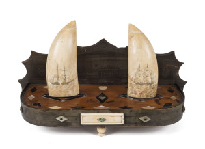 A Colonial scrimshaw desk set comprising of two sperm whale teeth engraved with tallships standing on a baleen and timber base inlaid with mother of pearl and tortoiseshell and adorned with whale bone. The baleen back plate engraved with a fine architectu