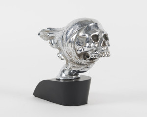 Skull car mascot, chrome on later ebonized timber base, circa 1950, mascot 14cm long