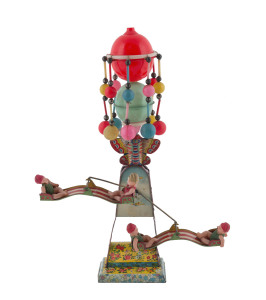 Windup tinplate double swing with four celluloid riders, mounted on a tower topped with rotating celluloid balls and small metal bells; the drive mechanism hidden behind metal plates with transfer printed early aeroplanes and an airship with Japanese live