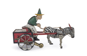 GERMAN LITHOGRAPHED TIN TOY "ZIKRA" BY LEHMANN Pulling a two-wheeled red cart with decorated wheels is a curious animal,the zebra-horse cross-bread Zebroid. A Mexican man is seated on the cart. When coil-spring wound, the man pulls on the reins, causing the unhappy zebroid to buck back and forth, his ears moving up and down, and thus causing the man to bounce up and down; the cart reluctantly moves forward. Marked Lehmann; circa 1925.