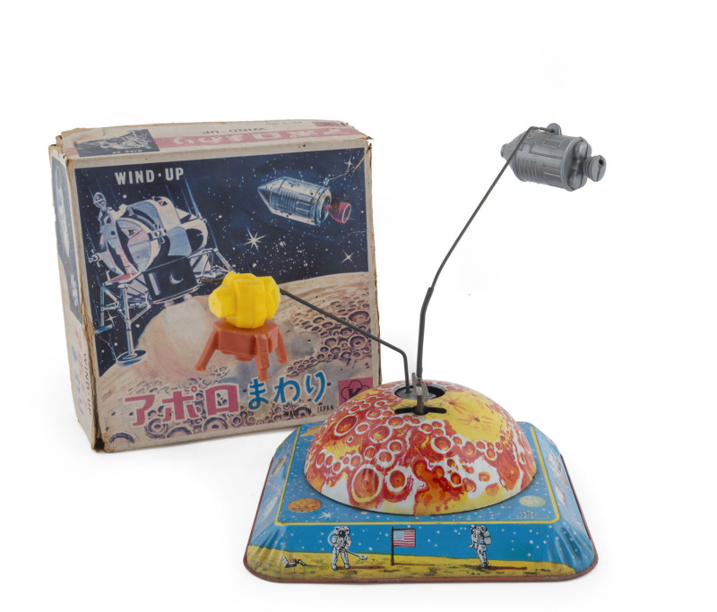 Wind-up tinplate and plastic Lunar orbiter and landing module which rotate around the lunar surface on a base with lithographed images of planets, moons and space craft; by Kokyo, Japan. Clearly made around 1969, the time of the Apollo Moon Landing. With