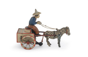 GERMAN LITHOGRAPHED TIN TOY "NA-NU" BY LEHMANN Pulling a two-wheeled cart with red trim is a curious animal, the zebra-horse cross-breed Zebroid. A man with blue shirt, brown pants and tall hat is seated on the cart. When the coil - spring is wound, the zebroid lurches forward, bucking and ears flapping while the man bounces up and down in the seat, attempting to hold him in with the reins. Length: 18.5cm (7.25"). {See also Lot......for another version of this toy}.