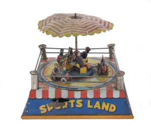 "Sports Land" wind-up tinplate carousel toy by C.K. (Japan), with three cars, each with two occupants, rotating on a circular track below below a striped scalloped umbrella, with a further three men seated around the the central umbrella pole, only the ce