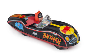 MASUDAYA / MODERN TOYS BATMOBILE. This circa 1960s Batmobile is tinplate litho, with rubber, friction driven wheels and a vinyl Batman driving with his vinyl cape flapping in the wind behind him. Length: 32cm (12.5").