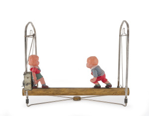 Two celluloid children attempting to remain upright on a swinging clockwork log; the frame in metal, the log tin lithographed. Each child with "JAPAN" and a quartered circle logo on their backs. Unknown maker. Length: 34cm (13.5").