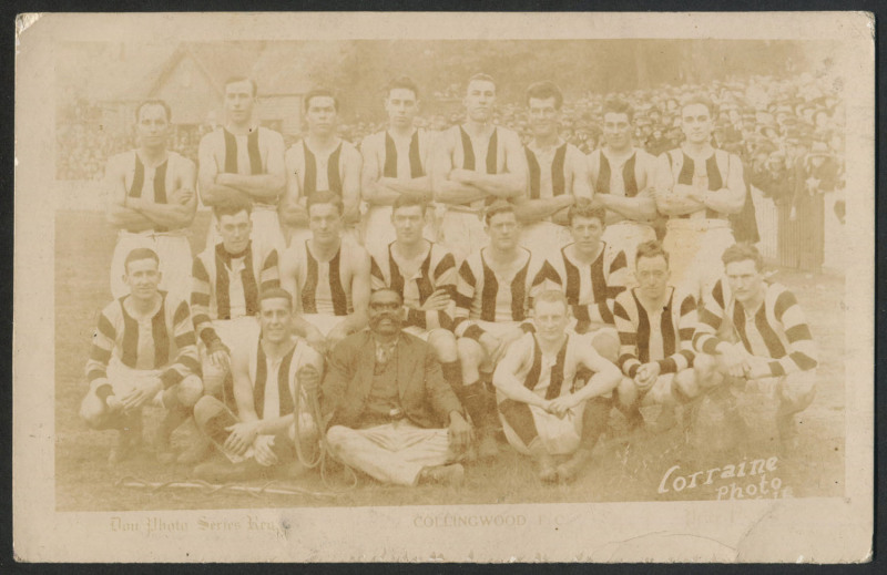 1924 COLLINGWOOD TEAM PHOTO: Don Photo Series (Lorraine Photo) postcard with a besuited indigenous gentleman holding a rope sat in the front row; somewhat faded. [Indigenous Australians sometimes provided half-time entertainment at games, culturally-based