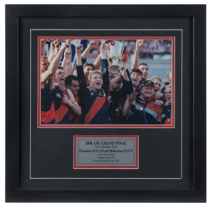 ESSENDON: '2000 AFL Grand Final" celebratory team photograph with commemorative plaque beneath; also 2001 Gary Moorcroft triptych of photos showing the "AFL Mark of the Year" sequence, centre photo signed by Moorcroft; both items framed & glazed, overall 45x45cm & 30x49.5cm respectively. (2)