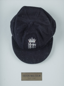 DEVON MALCOLM'S ENGLAND HOME TEST TEAM CAP, navy blue wool with embroidered Crown over three lions on front, with "D.M." to inside label. Very fine condition. Attractively framed.