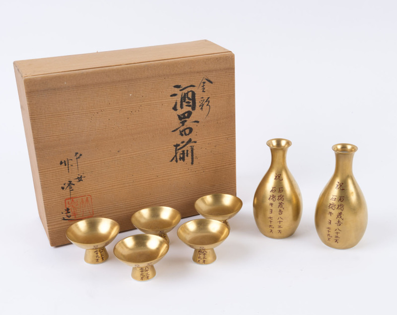 A Japanese seven piece gilded porcelain sake set with red calligraphy decoration, in original wooden box, ​the bottles 11.5cm high