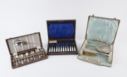 A sterling silver three piece vanity set in case, an antique fruit cutlery set in case, mother of pearl and silver plate; plus a dessert cutlery set in box, (3 items)