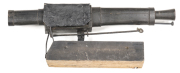 AUST COLONIAL PERIOD CONVICT PERC TRAP GUN: 1 3/8" at the muzzle; 15" iron barrel; barrel & lock encased in wood & secured by 2 wide iron bands; plain lock & hammer; activated by a lever underneath the body of the gun, when someone trips the wires; drk br