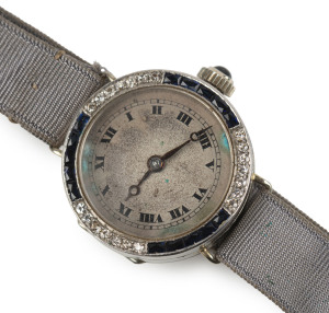 A ladies cocktail watch, 18th white gold case with diamond and sapphire bezel, Roman numerals and silk band with sapphire studded crown, early 20th century, 2.4cm wide