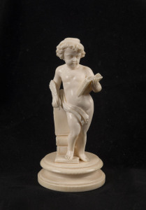 A Dieppe carved ivory statue of a naked boy with quill and books, 19th century, 11cm high