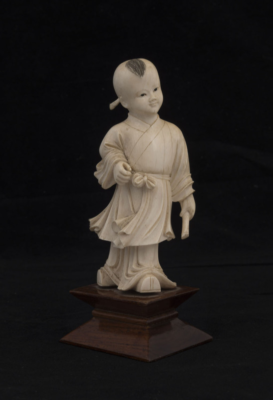 A Chinese carved ivory statue of a boy on wooden stand, early 20th century, ​12cm high, 15.5cm overall