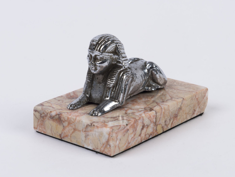 A sphinx chromed metal car mascot on pink marble plinth, circa 1920s ​8cm high, 11.5cm wide overall