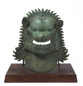 A Balinese bronze mask on wooden base, early 20th century, ​47cm high, 46cm wide, 22cm deep overall