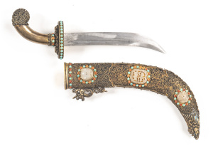 BURMESE SINGLE EDGED DRESS KNIFE: vg 7" slightly curved blade with groove to back edge; brass oval guard set with turquoise & semi-precious stones; plain brass hilt with a floral patterned pommel; v. ornate brass over wood scabbard with a mythical figured