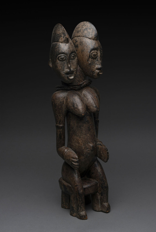 A double headed female seated figure, carved wood, cloth aand remains of painted finish, Senufo tribe, Ivory Coast, 54cm high