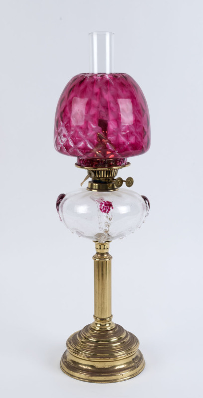 An antique oil lamp with brass base and column, clear glass font with cranberry prunts, brass double burner and chimney (later shade), has been electrified (wires cut), 68cm high