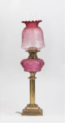 An antique oil lamp with brass base and column, ruby glass font, brass double burner and chimney (later shade), has been electrified (wires cut), 68cm high