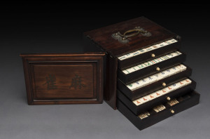 A Chinese marine ivory and bone Mah-jong set in a hardwood table cabinet with a sliding door opening to reveal five drawers with a complete set of hand painted pieces. The hardwood box has double bronze handles. Chinese character marks with the original owner's name on the back inlaid in mother of pearl, circa 1920, 25cm wide