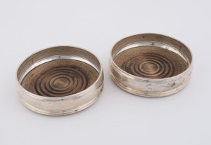 A pair of sterling silver champagne bottle coasters, of plain form with wood inlaid bases, by Mills & Hersey, London, circa 1977, 13cm diameter.