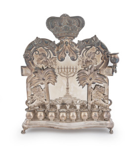A silver plate Hannukah oil lamp of Polish origin, decorated with a menorah, applied figures of rampant lions, palm trees and leaves beneath a Torah crown, made by Norblin & Co, Warsaw, early 20th century, (lacks one perforated burner cover), 29cm high.