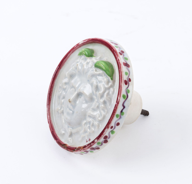 An antique French porcelain furniture knob with Medusa head motif, 18th/19th century, 9.5cm diameter